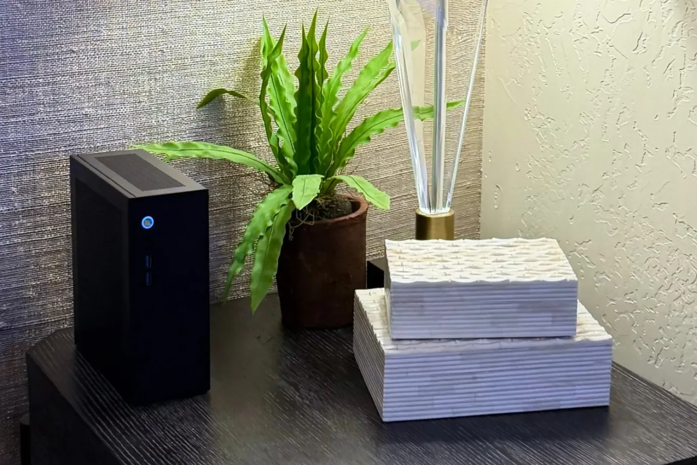 A black Companion computer on a dark side table beside a potted plant and two stacked textured boxes