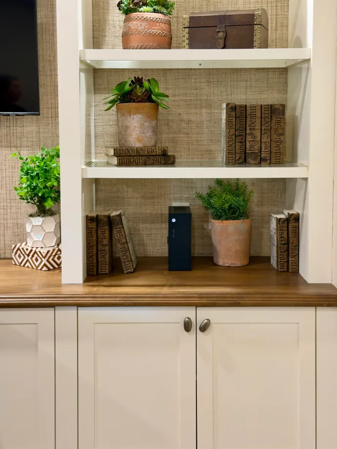 A small black Companion computer on a shelf in a built-in bookcase, among books and potted plants