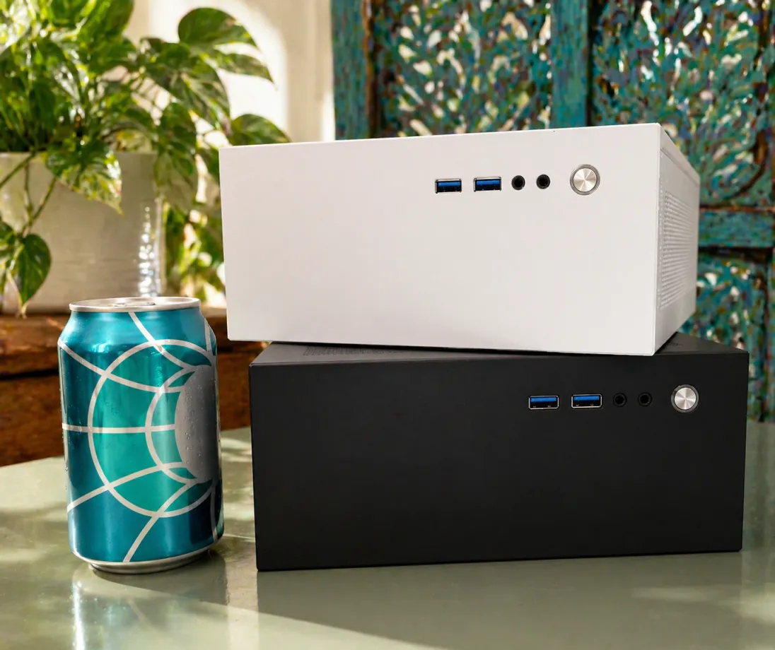 A white Companion computer stacked on a black one beside a teal patterned drink can, with a plant and a carved teal screen behind