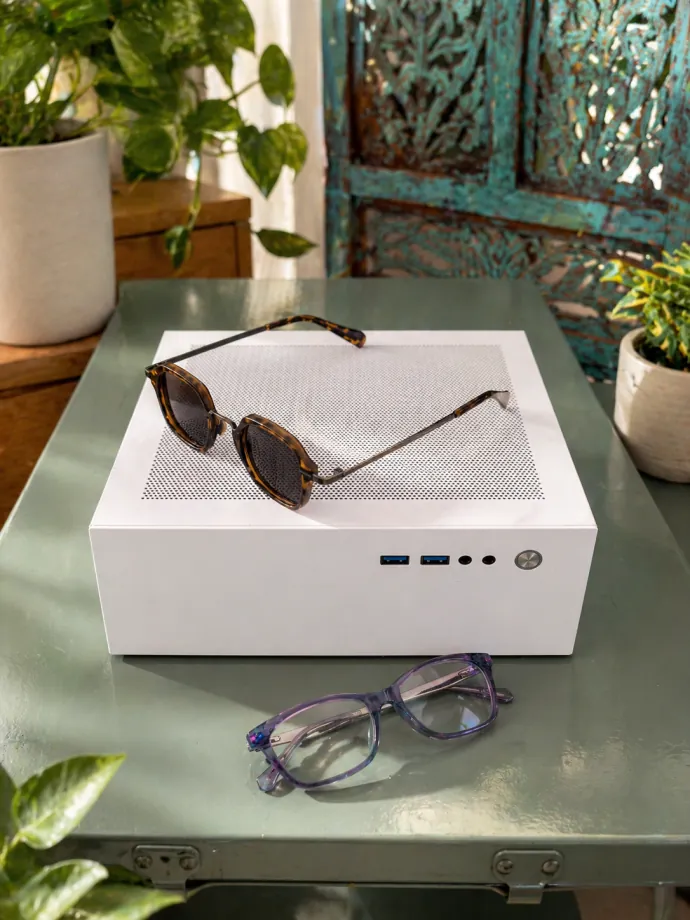 A white Companion computer on a glass table with a pair of sunglasses resting on top and eyeglasses in front, among plants