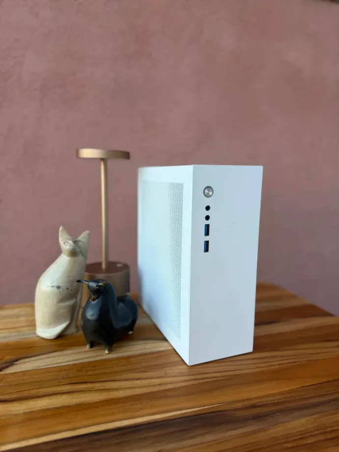 A white Companion computer standing on a wooden table against a mauve wall, next to a ceramic cat, a small black figurine and a brass table lamp